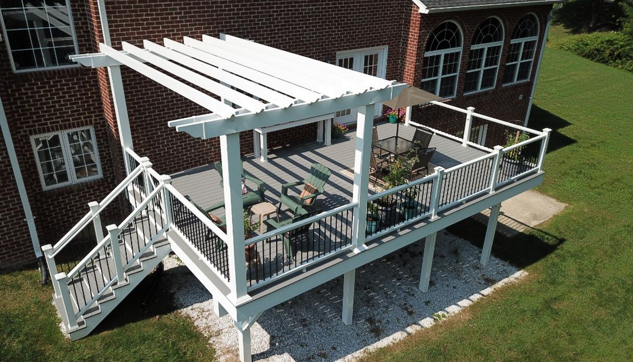 Trex Select Pebble Gray Composite Deck with Trex Composite Railing with black aluminum balusters and a White Vinyl Pergola