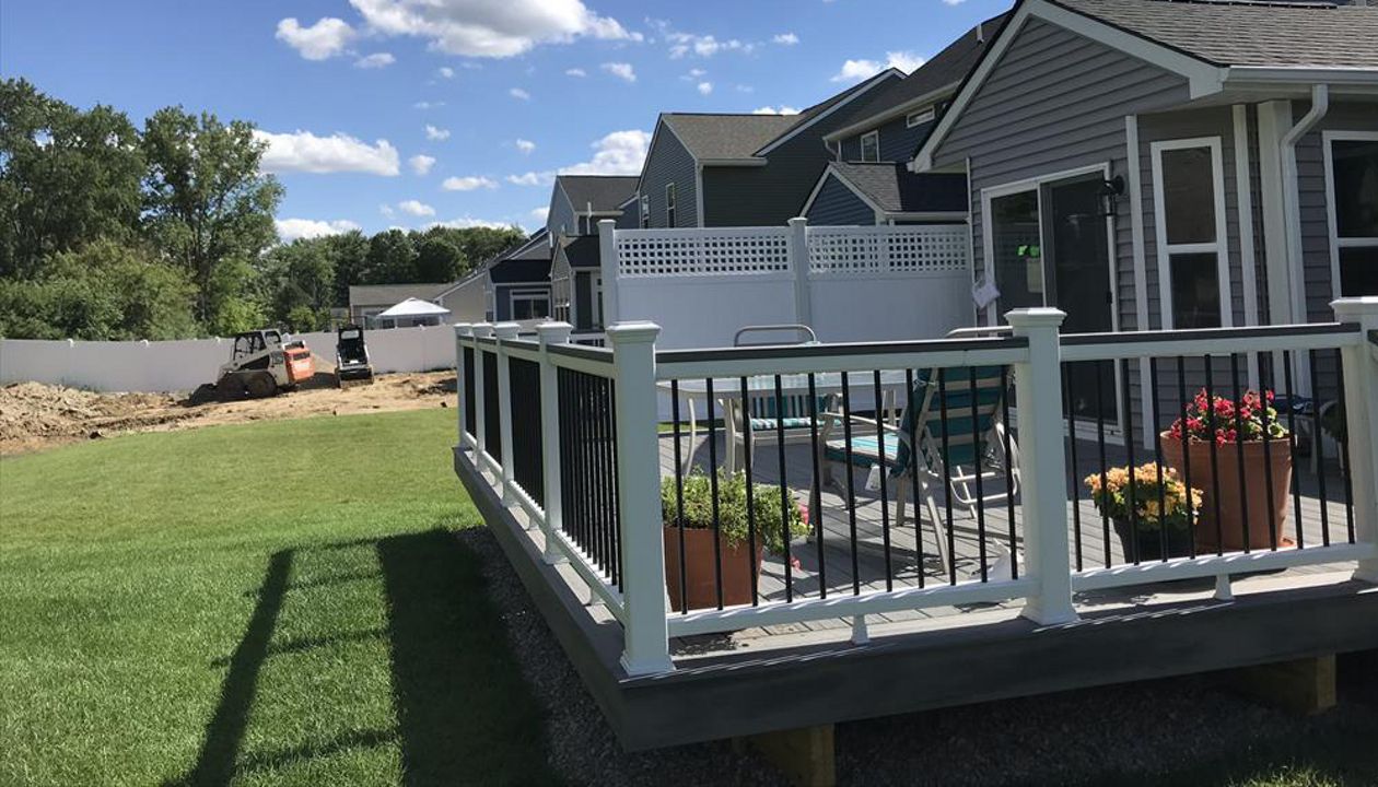 Deck in New Hudson, MI., constructed out of Trex Transcend Tropical decking in Island Mist and complimented by Classic White Trex railing with black balusters and Classic White privacy wall.