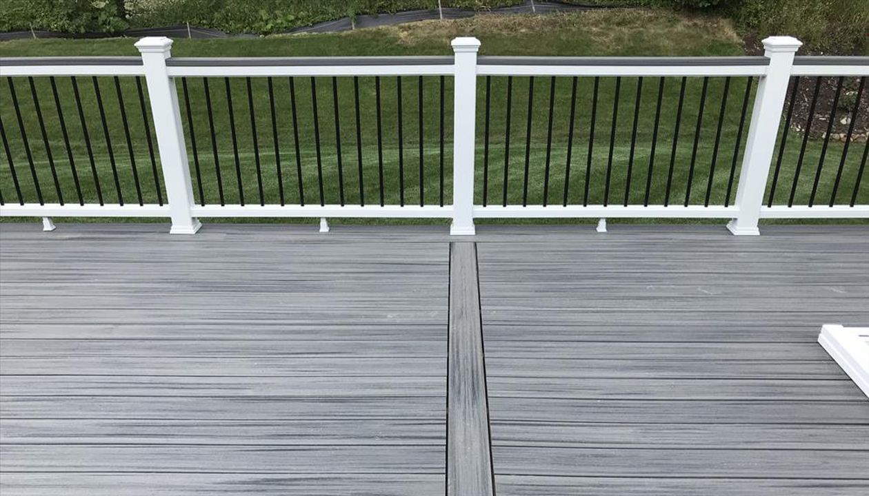 Deck in New Hudson, MI., constructed out of Trex Transcend Tropical decking in Island Mist and complimented by Classic White Trex railing with black balusters and Classic White privacy wall.