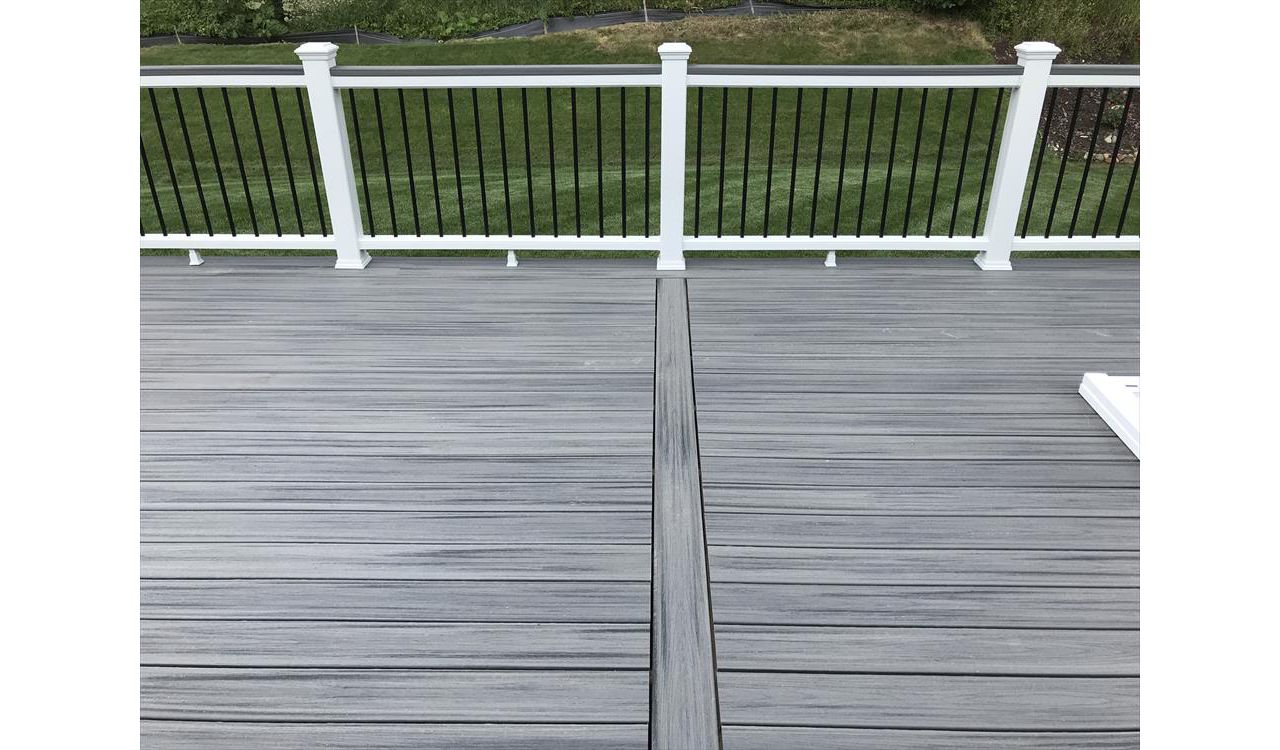 Deck in New Hudson, MI., constructed out of Trex Transcend Tropical decking in Island Mist and complimented by Classic White Trex railing with black balusters and Classic White privacy wall.