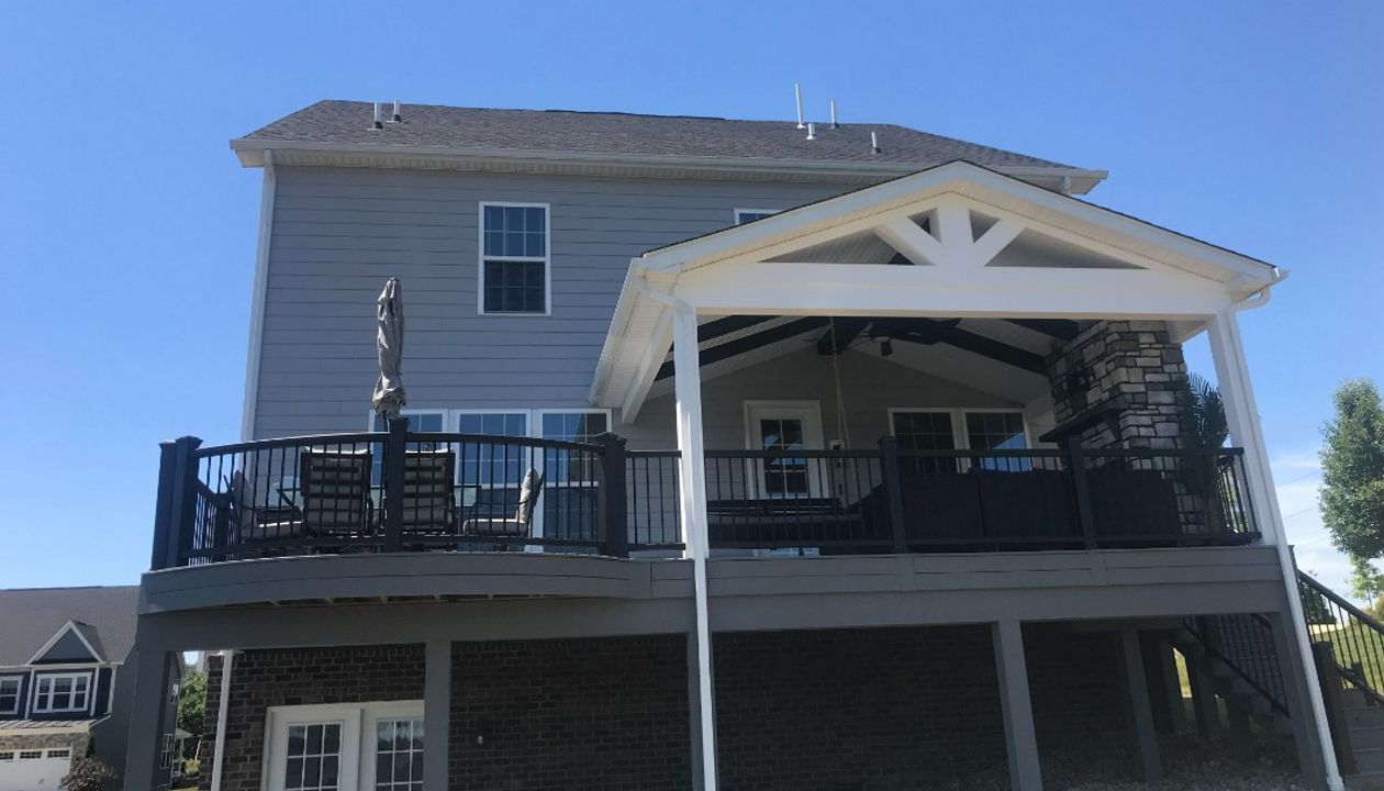 Partially covered curved Pebble Gray deck. Stone veneer gas fireplace completes this outdoor living space
