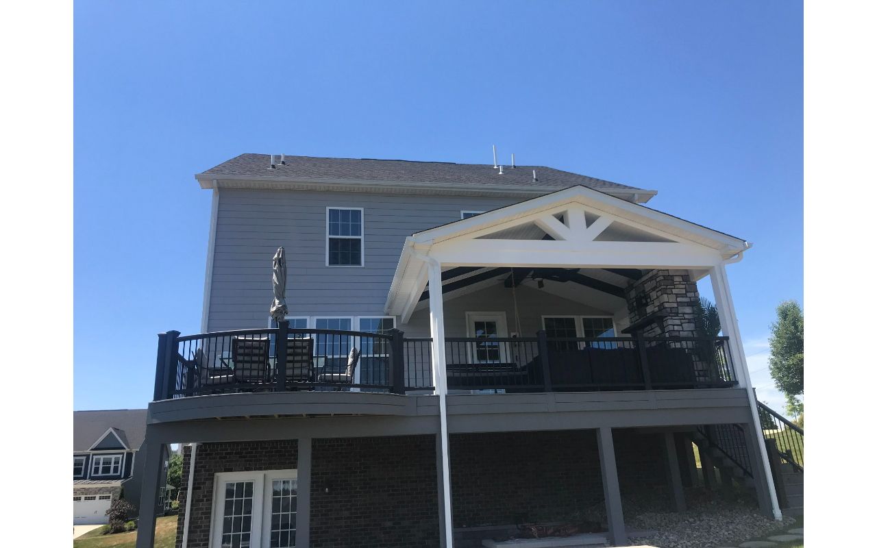 Partially covered curved Pebble Gray deck. Stone veneer gas fireplace completes this outdoor living space