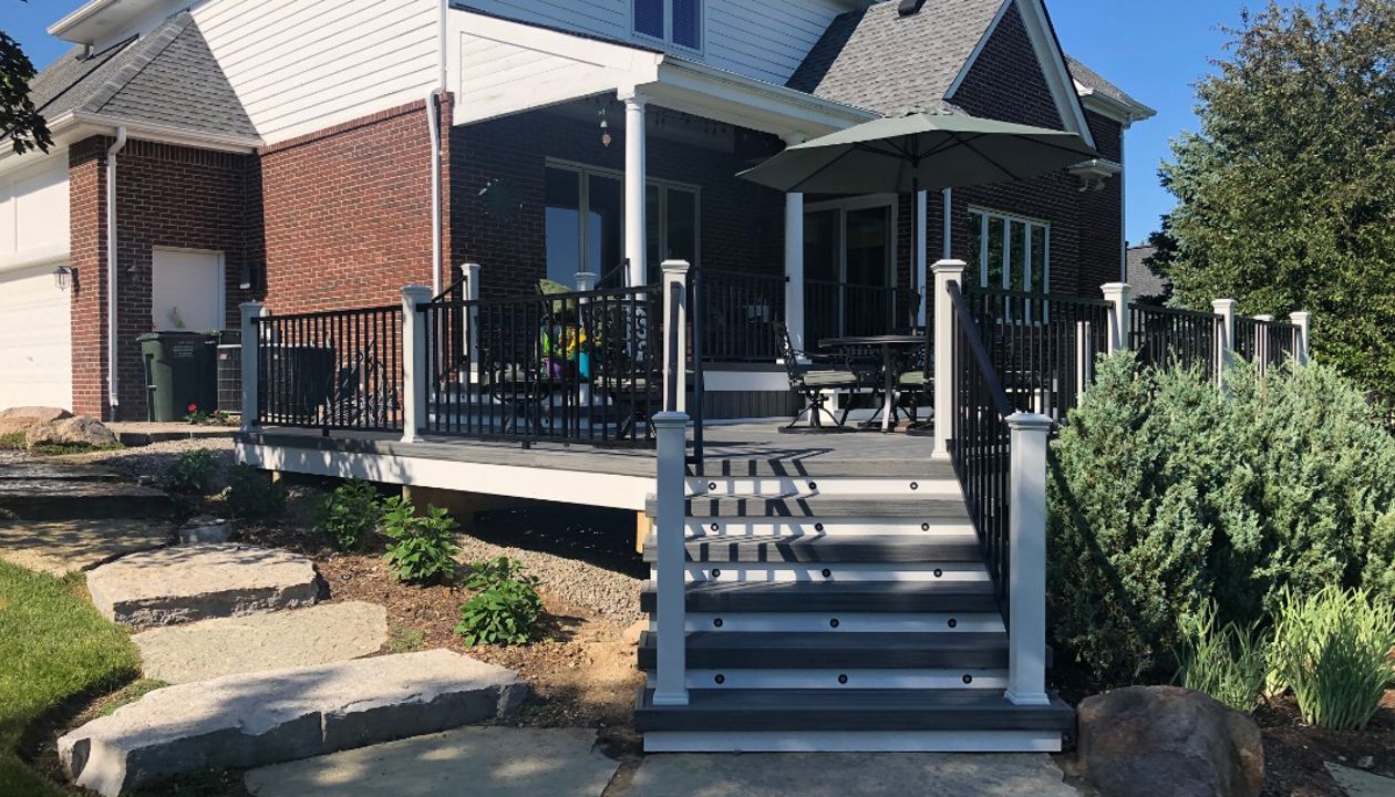 Large TREX Island Mist deck with Black Signature rail, White Transcends post, cap, skirt, and fascia with elevated covered porch