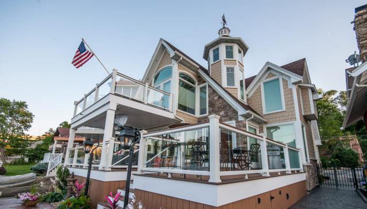 Lake house deck featuring Trex Enhance Beach Dune decking with white Trex Transcend universal railing with tempered glass. This 2-story deck has a drainage system along with a custom spiral staircase. Skirting and Post wraps give an elegant touch.
