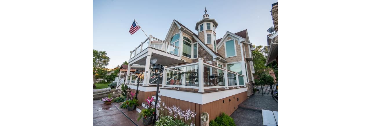 Lake house deck featuring Trex Enhance Beach Dune decking with white Trex Transcend universal railing with tempered glass. This 2-story deck has a drainage system along with a custom spiral staircase. Skirting and Post wraps give an elegant touch.