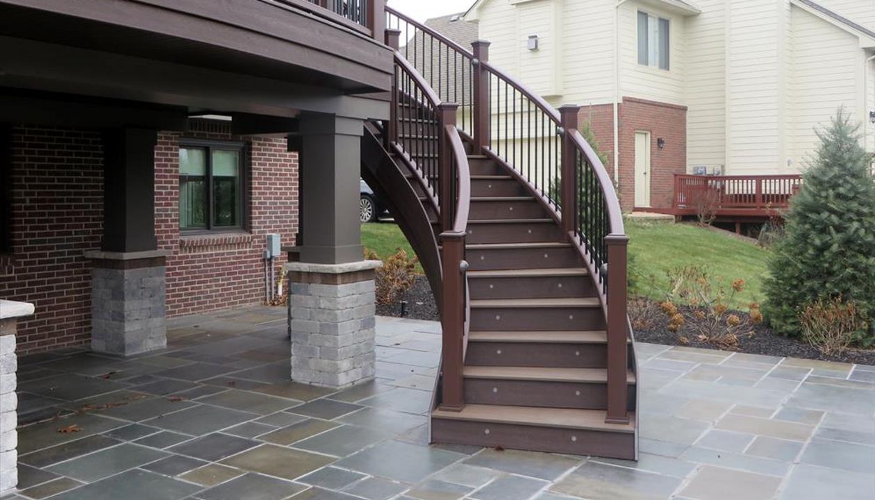 This deck in Plymouth, MI has fire pit Trex transcends decking with a vintage lantern border. The custom curve rail and stairs make this deck stand out.