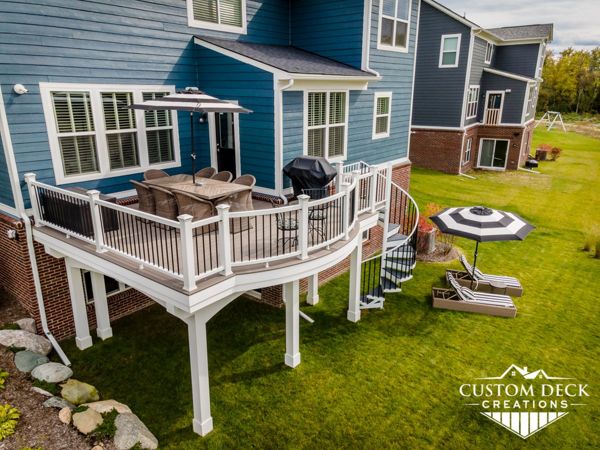 Trex Enhance Naturals Rocky Harbor decking with custom-curved white Trex Select composite railing and black round aluminum balusters. Finished ceiling with Trex RainEscape and custom Trex spiral staircase.