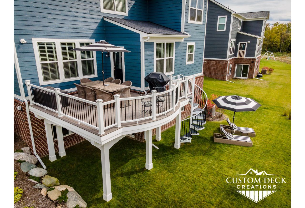 Trex Enhance Naturals Rocky Harbor decking with custom-curved white Trex Select composite railing and black round aluminum balusters. Finished ceiling with Trex RainEscape and custom Trex spiral staircase.