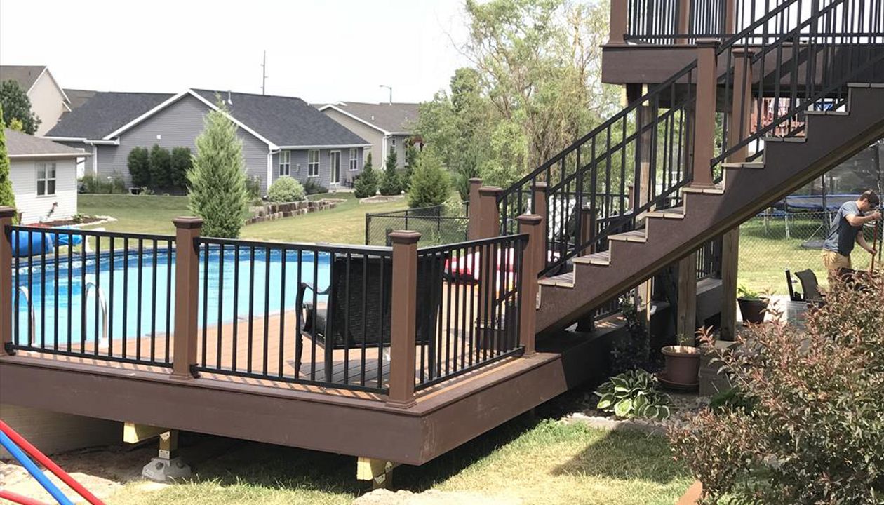 Customized decks done right by GE Contracting LLC. Vintage lantern rail posts with cap lights make the evenings much brighter for a swim. Signature black aluminum rails. Trex select Saddle inner boards and woodland brown accents. Make for a beautiful deck