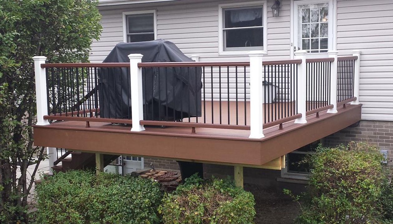 Trex Enhance decking in Saddle with a Fire Pit border. Railings have Fire Pit top and bottom rails with Classic White posts and caps and black round aluminum balusters.