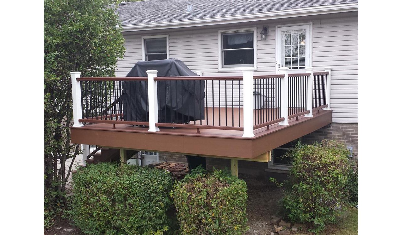 Trex Enhance decking in Saddle with a Fire Pit border. Railings have Fire Pit top and bottom rails with Classic White posts and caps and black round aluminum balusters.