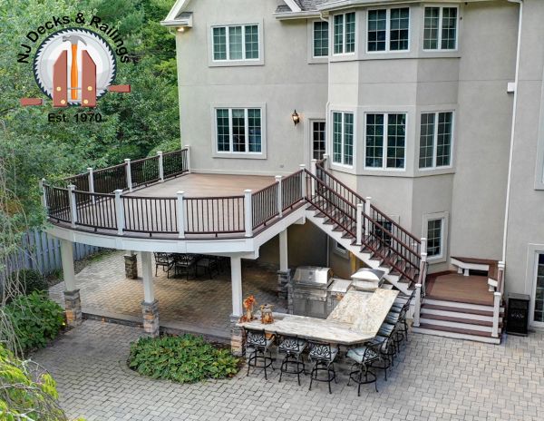 Curved edge deck using Trex Transcend Spiced Rum decking with Vintage Lantern border and railings between white posts. Also includes a drainage system and ceiling below complete with fans, heaters and speakers.