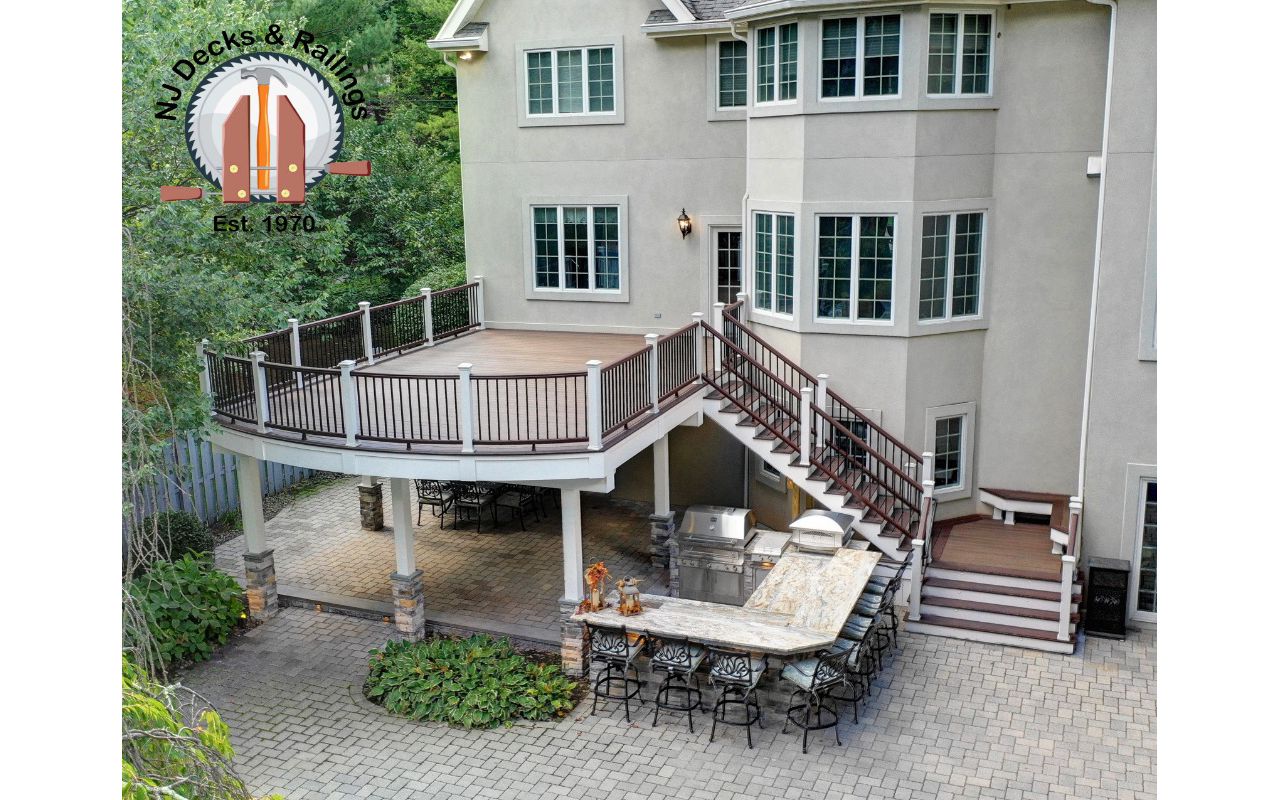 Curved edge deck using Trex Transcend Spiced Rum decking with Vintage Lantern border and railings between white posts. Also includes a drainage system and ceiling below complete with fans, heaters and speakers.