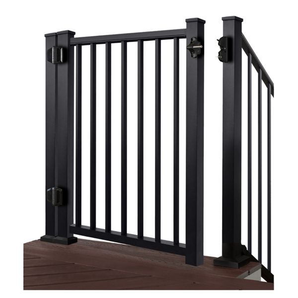 A black metal safety gate is installed between two sturdy posts on a raised deck. The gate features evenly spaced vertical bars and secure hinge hardware on one side. Brown wooden decking is visible beneath the gate, contrasting with the dark frame. The image is isolated on a white background, emphasizing the gate’s structure and clean lines.