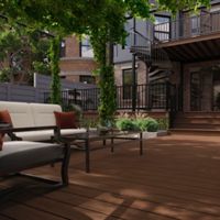 A contemporary outdoor patio features cushioned seating and a glass coffee table on a spacious wooden deck. Lush green vines climb pergola posts, creating a shaded, inviting atmosphere. In the background, a black metal spiral staircase leads to an upper balcony, with brick walls and large windows adding architectural interest. The setting is tranquil and ideal for relaxation or social gatherings.