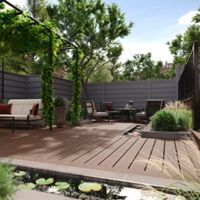 A spacious backyard patio features contemporary outdoor furniture, including cushioned sofas and chairs arranged for relaxation. The setting includes a wooden deck, lush greenery, and a small pond with lily pads in the foreground. Vertical trellises with climbing plants add shade and visual interest, while privacy fencing surrounds the area. The overall mood is tranquil and inviting, ideal for outdoor gatherings.