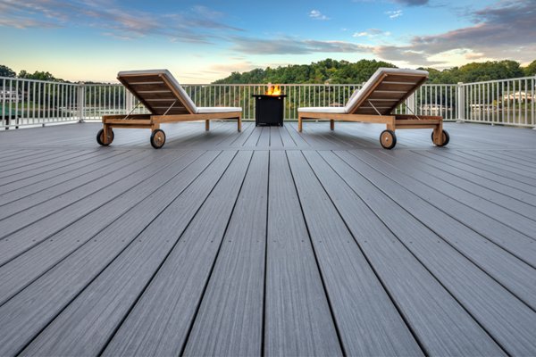 A Trex Signature Whidbey deck from a low angle looking onto two pieces of deck furniture and a fire pit as the chairs overlook a beautiful river and greenery on the otherside of the river.