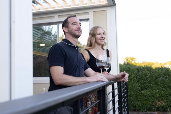 A couple standing at a Trex Signature Rod Railing with wine in hand and smiling off into the distance. 