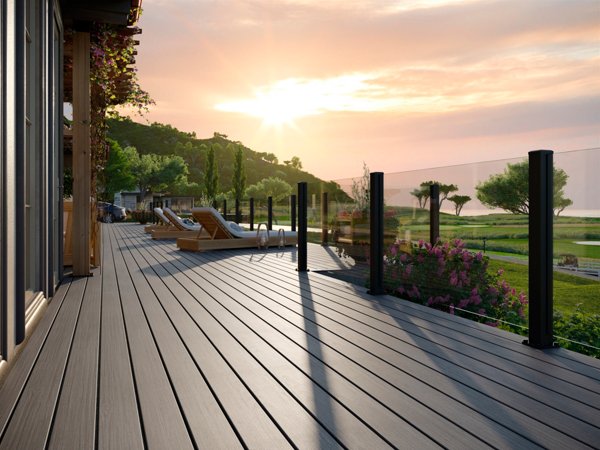 A Trex deck in the color Whidbey at sunset looking over a gorgeous park that extends toward the water, with the deck framed by the sleek and luxurious looking Trex Signature X-Series Frameless Glass railing.