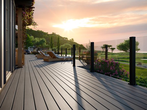 A Trex deck in the color Whidbey at sunset looking over a gorgeous park that extends toward the water, with the deck framed by the sleek and luxurious looking Trex Signature X-Series Frameless Glass railing.