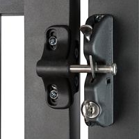 A detailed view of a contemporary metal gate latch is shown in a locked position. The latch features a robust design with visible screws and a cylindrical locking mechanism. The setting appears to be an industrial or residential gate, with a focus on the hardware's durability and security. The color palette is primarily matte black and metallic silver, emphasizing a modern, utilitarian style.