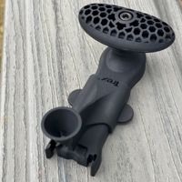 A black Trek bicycle mount component is displayed on a weathered wooden surface. The part features a honeycomb-patterned oval platform and a cylindrical attachment point. The Trek logo is clearly visible on the body of the component. The image is shot outdoors in natural light, highlighting the matte finish and detailed design.