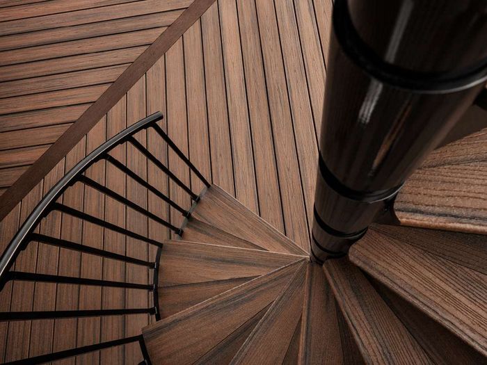 This image features a spiral staircase constructed from dark wood, viewed from above for a dramatic geometric effect. The staircase is complemented by a sleek black metal railing and a central supporting column. The wood grain and angular lines create a modern, visually striking pattern. No visible text, numbers, or logos are present in the image.