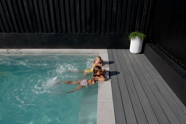 Two children swimming and smiling in a pool that is built onto a Trex Island Mist pool deck. 