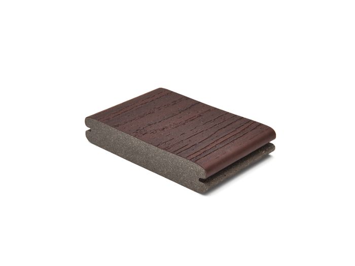 A single piece of brown composite decking board is displayed against a plain white background. The board features a wood grain texture on the top surface and a grooved edge, suggesting it is designed for easy installation. The sample highlights the material's layered construction and rich, dark brown color. No visible text, numbers, or logos are present in the image.