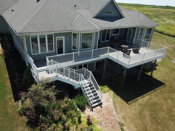 Home with a large deck with white railing and classic stairs leading to a garden below.