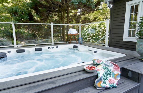 Hot tub built into a grey composite deck with glass railings in the background