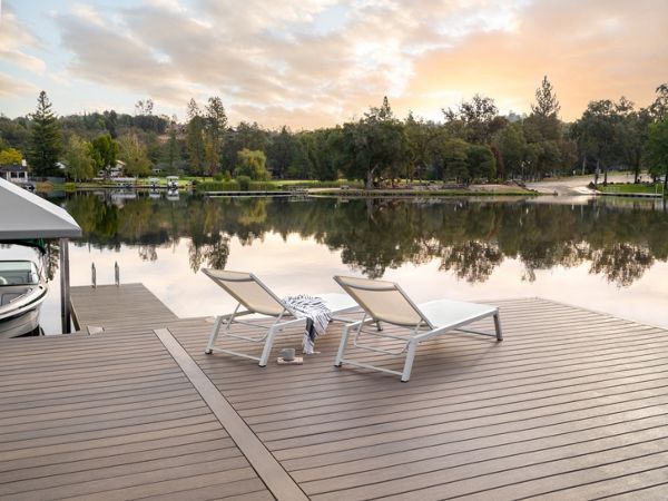 Two chairs on a dock made of Trex decking with the sun setting in the horizon over the water.