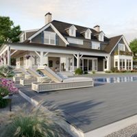 A large modern farmhouse features a spacious outdoor area with a swimming pool and multiple lounge chairs. The setting is a landscaped backyard with flowering plants, a wooden deck, and an adjacent covered dining area. The house has white siding, dark roofing, and several dormer windows, creating a welcoming and upscale atmosphere. The scene is bright and tranquil, ideal for relaxation or entertaining guests.
