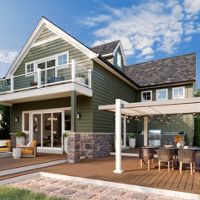 A contemporary two-story green house features a large wooden deck and an inviting outdoor dining space under a pergola. The setting includes comfortable seating areas, a barbecue grill, and a well-maintained garden, all under a bright blue sky with scattered clouds. The overall mood is relaxed and welcoming, with natural tones and modern design elements.