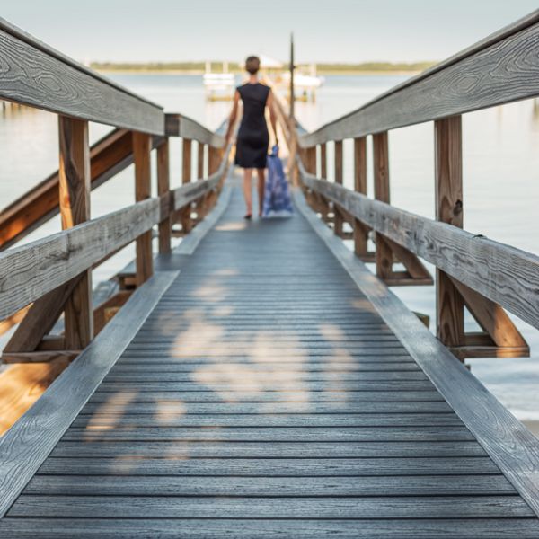 14. A person walking down a dock made of Trex decking as it leads to the shore.