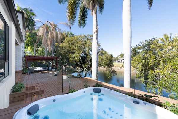 Hot tub built into a grey composite deck with glass railings in the background